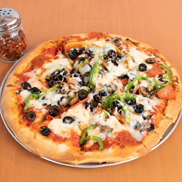 A whole Marri's Pizza with pepperoni, olives, green peppers, and mushrooms, next to a shaker of red pepper flakes.