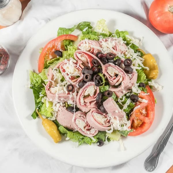 Marri's Pizza Italian salad with rolled meats, cheese, olives, tomatoes, and lettuce on a white plate.