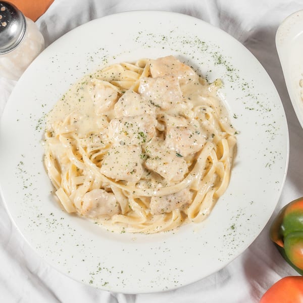 Creamy chicken fettuccine alfredo with parsley flakes on a white plate, with a cheese shaker nearby.