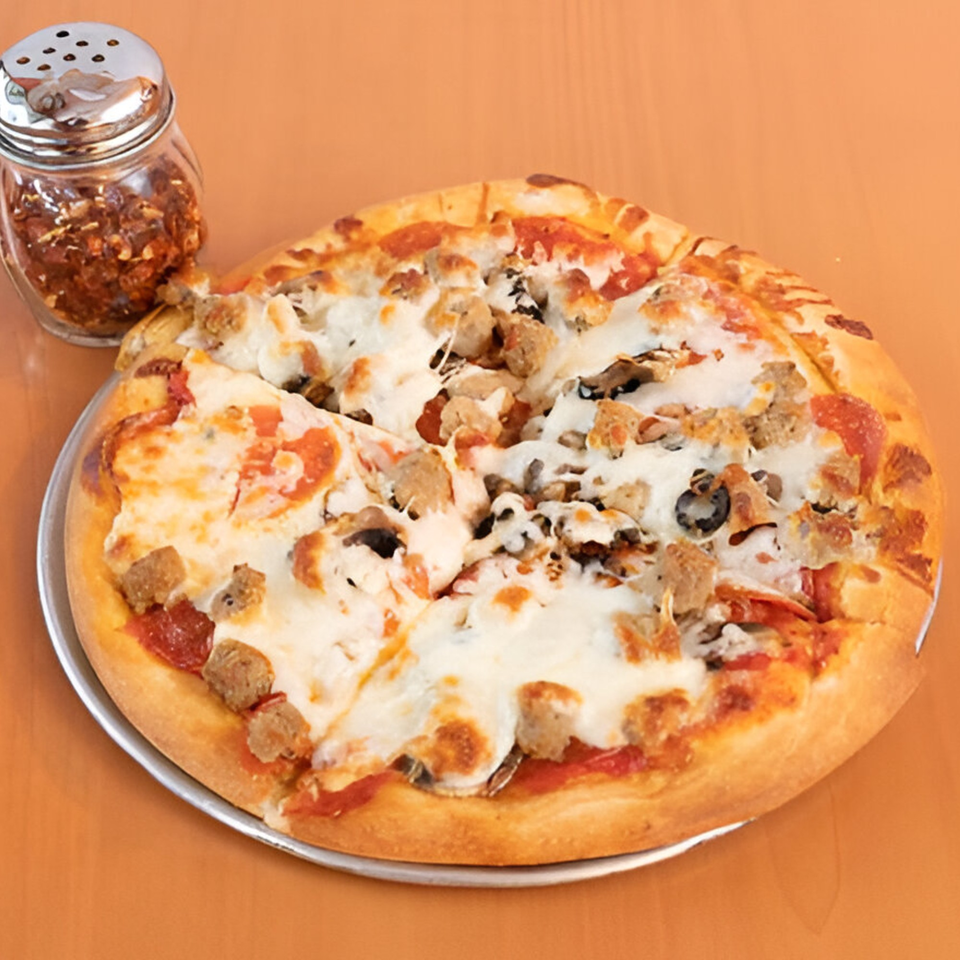 A Marri's Pizza Orange pizza with pepperoni, sausage, mushrooms, and olives, with a shaker of red pepper flakes.