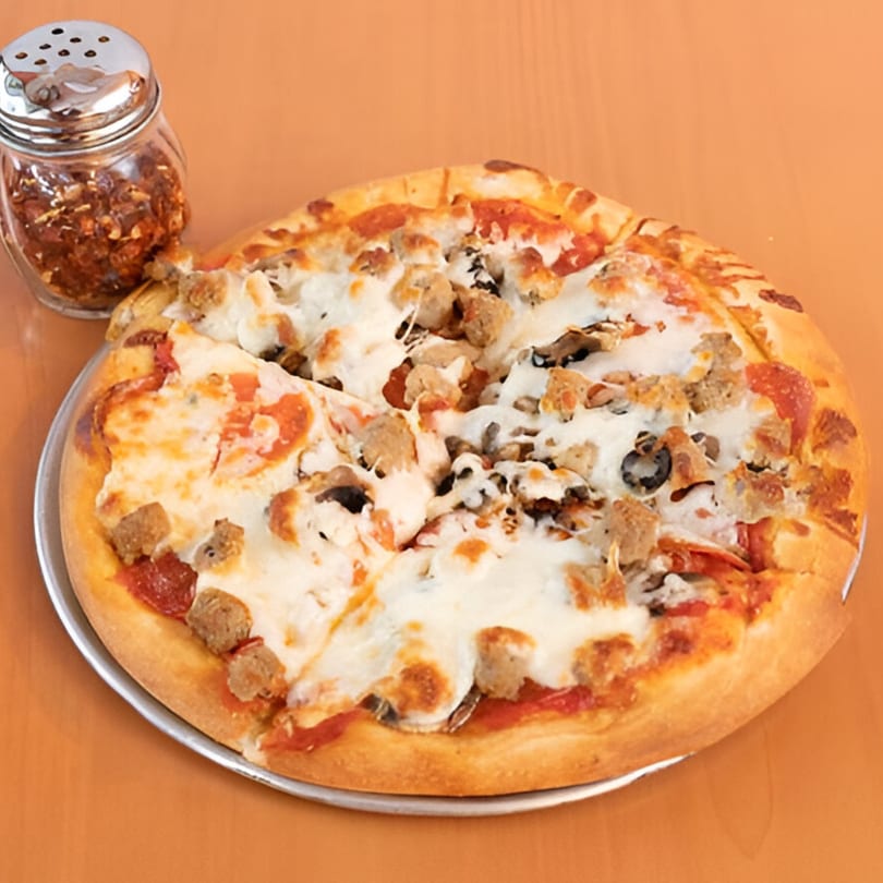 A Marri's Pizza Orange pizza with pepperoni, sausage, mushrooms, and olives, with a shaker of red pepper flakes.