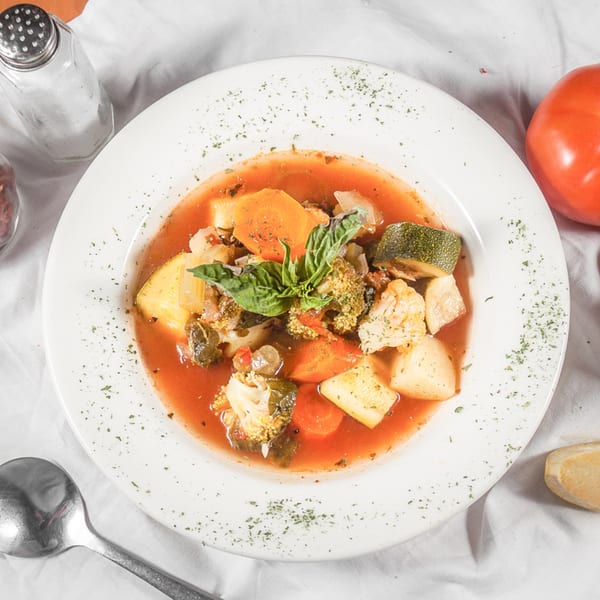 Hearty Italian vegetable soup with carrots, zucchini, potatoes, and basil in a white bowl.